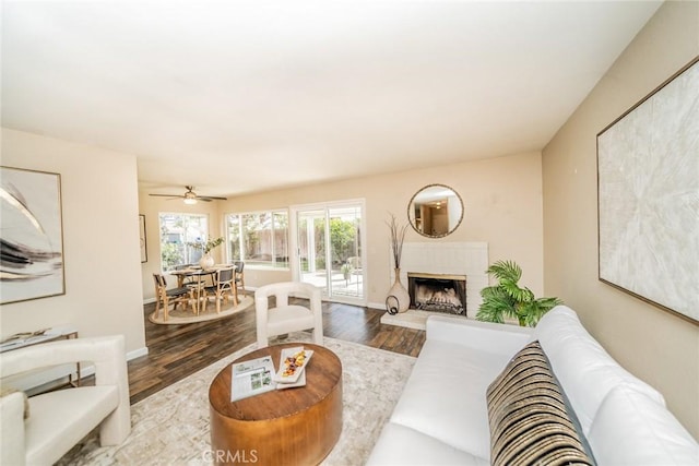 living area with a fireplace with raised hearth, baseboards, and wood finished floors