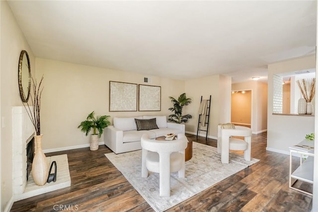 living room featuring a brick fireplace, wood finished floors, visible vents, and baseboards