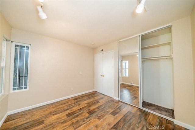 unfurnished bedroom featuring visible vents, wood finished floors, baseboards, and a closet