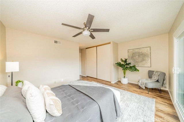 bedroom with light wood finished floors, visible vents, a closet, a textured ceiling, and a ceiling fan