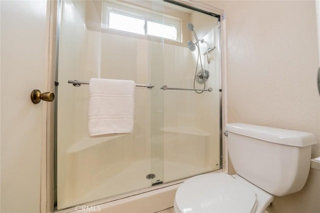 bathroom with toilet, a stall shower, and a textured wall