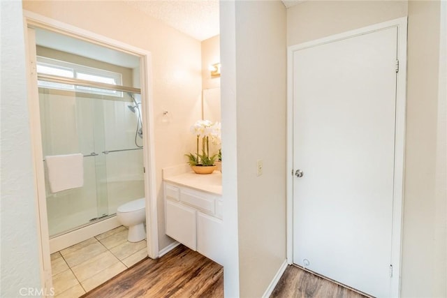 full bathroom with toilet, a stall shower, a baseboard heating unit, wood finished floors, and vanity