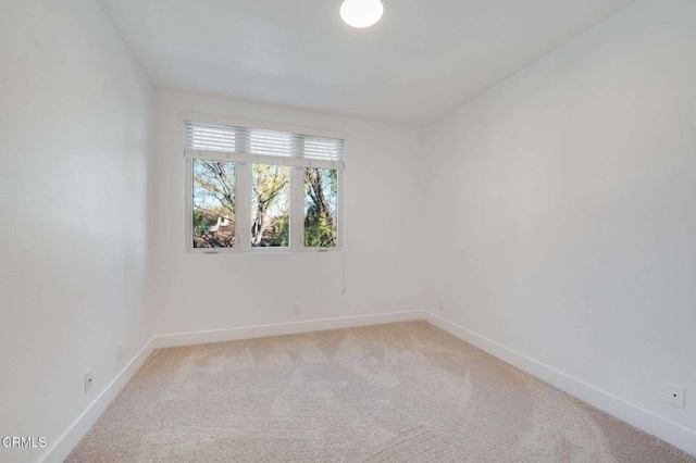 spare room with baseboards and light colored carpet