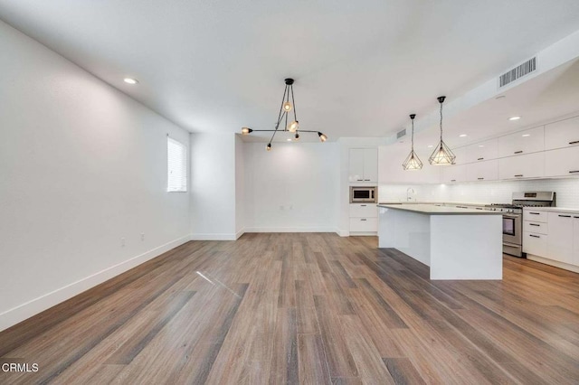 kitchen with white cabinets, decorative backsplash, wood finished floors, stainless steel appliances, and pendant lighting