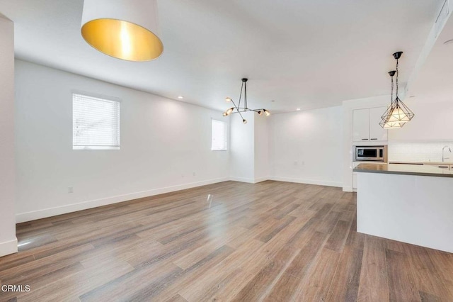 unfurnished living room featuring a notable chandelier, recessed lighting, a sink, wood finished floors, and baseboards