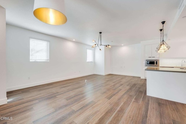 unfurnished living room with baseboards, a notable chandelier, a sink, and wood finished floors