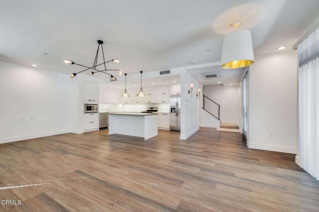 unfurnished living room featuring an inviting chandelier, wood finished floors, and visible vents