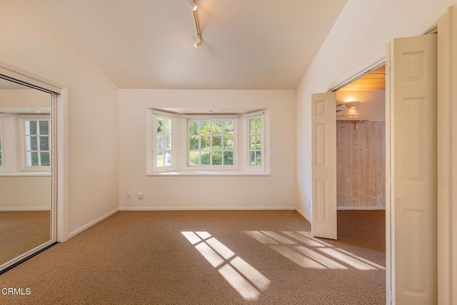 unfurnished bedroom with vaulted ceiling, rail lighting, carpet, and baseboards