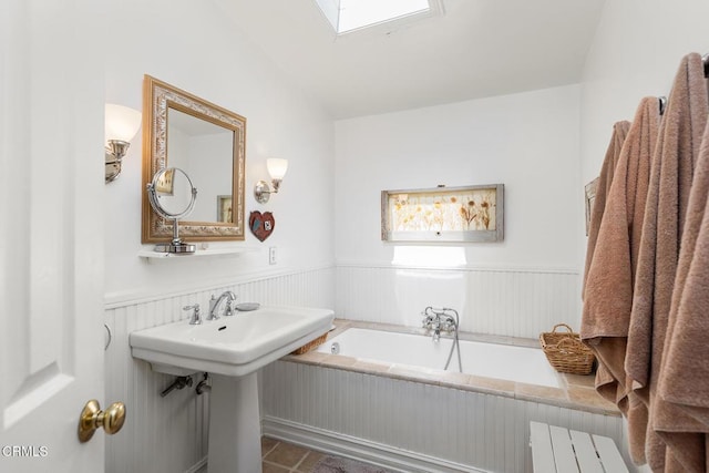 bathroom featuring a sink, a bath, and wainscoting