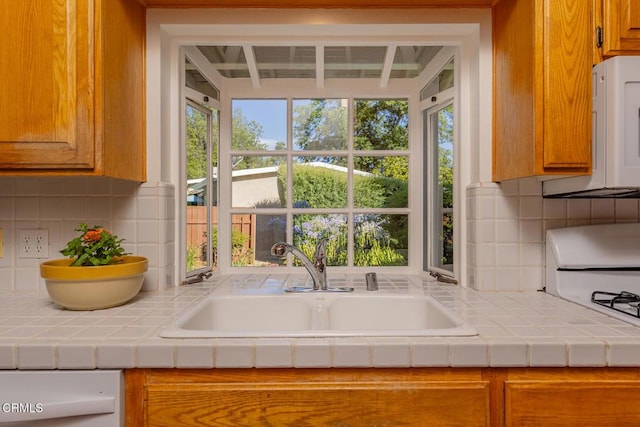 kitchen featuring white microwave, backsplash, tile countertops, brown cabinets, and a sink