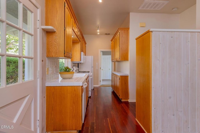 kitchen with baseboards, visible vents, dark wood-style flooring, decorative backsplash, and tile counters