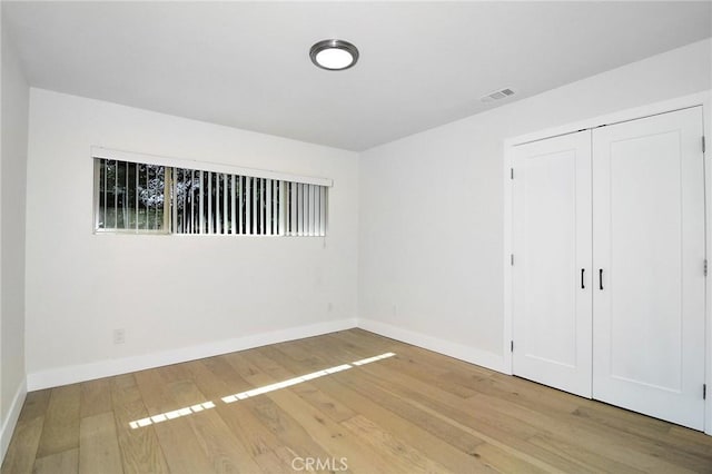 unfurnished bedroom with a closet, wood-type flooring, visible vents, and baseboards