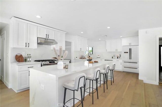 kitchen with stainless steel gas stove, a breakfast bar, white fridge, light wood-type flooring, and under cabinet range hood