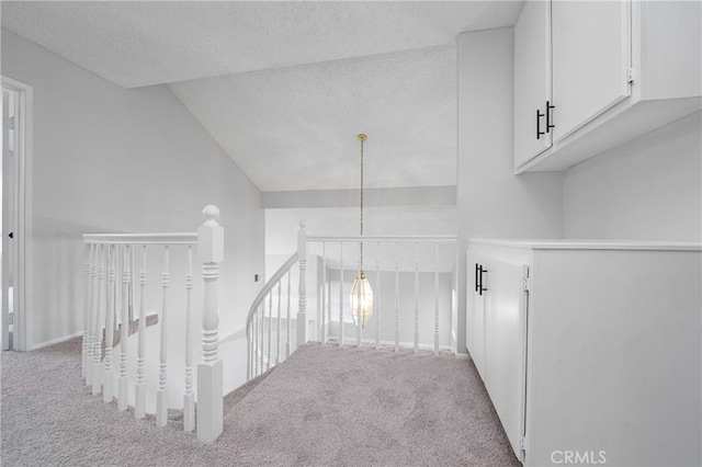 corridor with carpet floors, a textured ceiling, and an upstairs landing