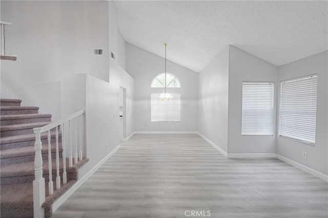 unfurnished dining area featuring stairway, wood finished floors, vaulted ceiling, a textured ceiling, and a chandelier