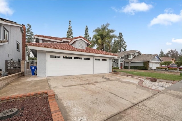 mediterranean / spanish house featuring an attached garage, a tiled roof, concrete driveway, a gate, and stucco siding