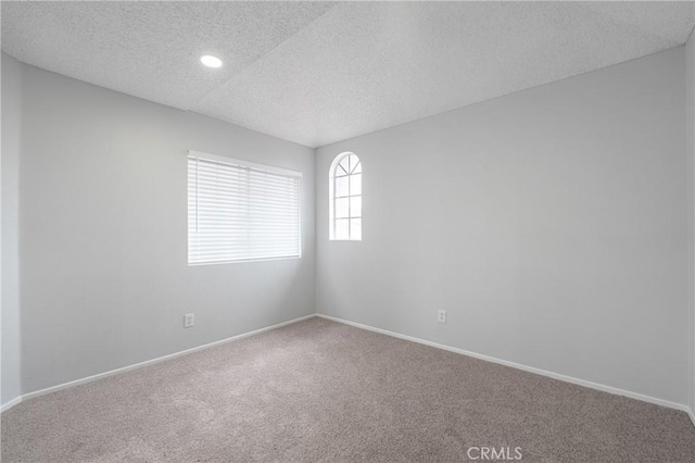 carpeted empty room featuring a textured ceiling and baseboards