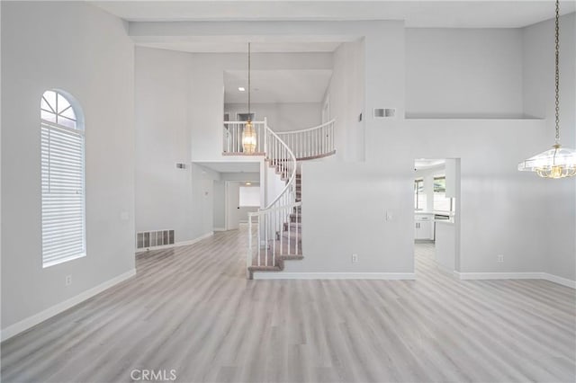 unfurnished living room with a chandelier, a high ceiling, visible vents, and baseboards