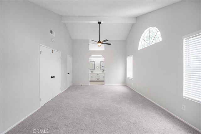 unfurnished living room featuring arched walkways, ceiling fan, beamed ceiling, and carpet flooring