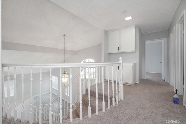 hallway with light carpet, vaulted ceiling, a textured ceiling, and an upstairs landing