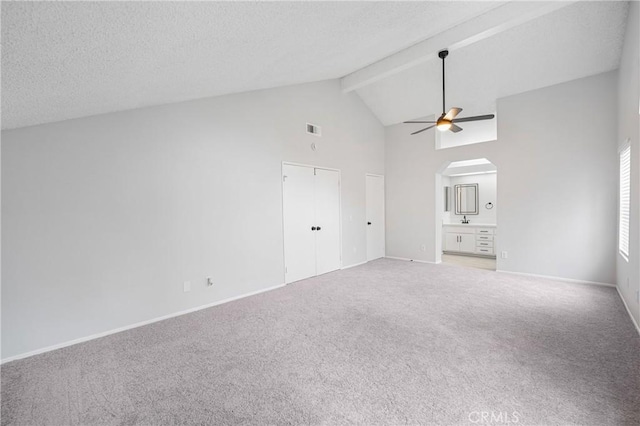 unfurnished bedroom with arched walkways, a textured ceiling, visible vents, beam ceiling, and carpet