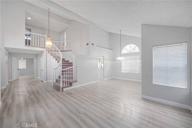 unfurnished living room featuring a textured ceiling, a notable chandelier, wood finished floors, baseboards, and stairway