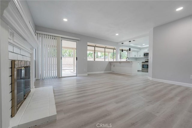 unfurnished living room featuring recessed lighting, a sink, light wood-style flooring, and baseboards