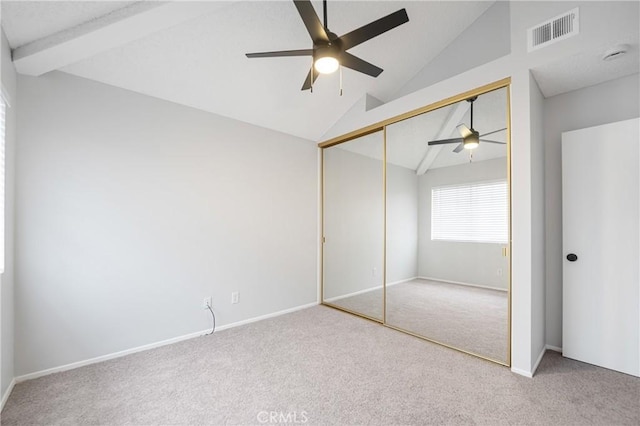 unfurnished bedroom featuring lofted ceiling, a closet, visible vents, carpet flooring, and ceiling fan