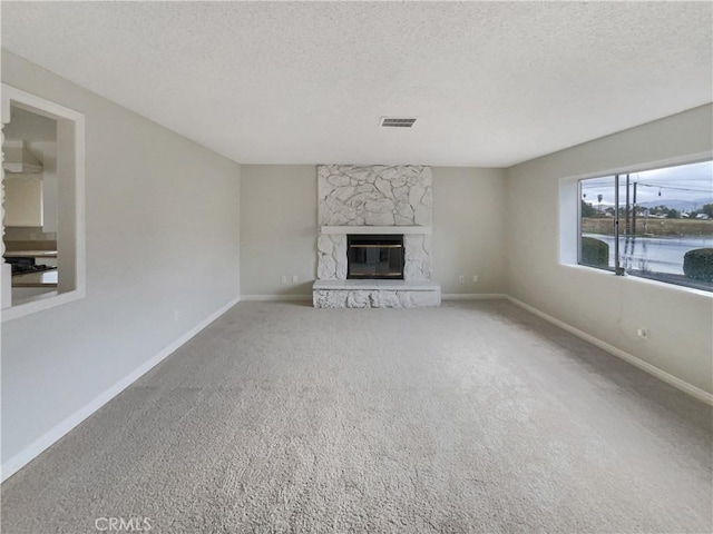 unfurnished living room featuring visible vents, carpet flooring, a stone fireplace, a textured ceiling, and baseboards