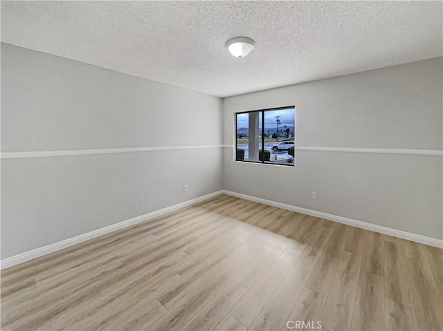 empty room with a textured ceiling, baseboards, and wood finished floors