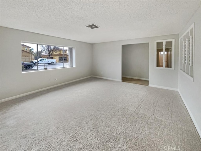 carpeted empty room featuring visible vents, a textured ceiling, and baseboards