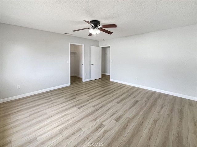 spare room featuring visible vents, light wood-style flooring, ceiling fan, a textured ceiling, and baseboards