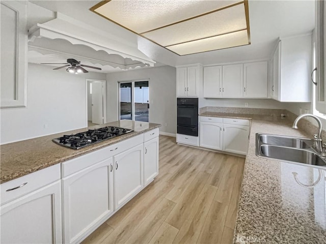 kitchen featuring stainless steel gas cooktop, light wood-style floors, white cabinetry, a sink, and black oven