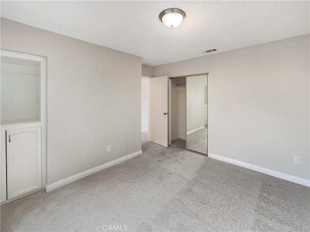 unfurnished bedroom with baseboards, visible vents, carpet, a textured ceiling, and a closet