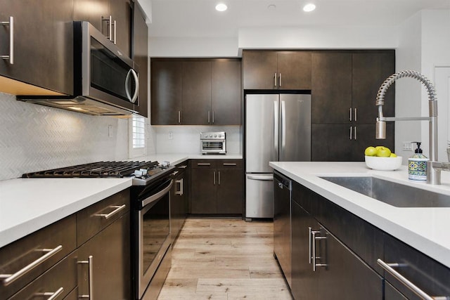 kitchen featuring light wood-style flooring, stainless steel appliances, a sink, dark brown cabinets, and light countertops