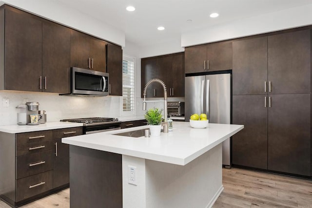 kitchen featuring light wood-type flooring, dark brown cabinets, stainless steel appliances, and a sink