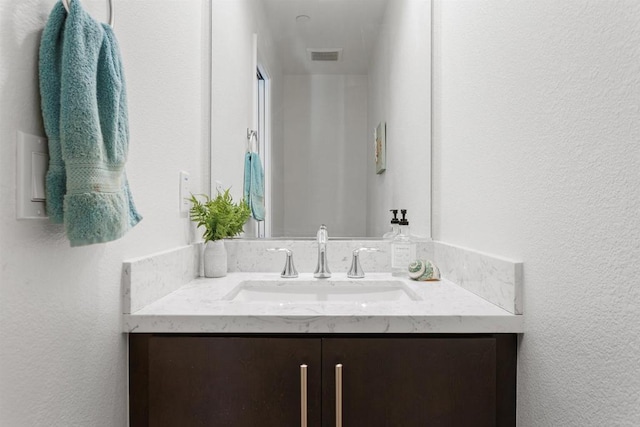 bathroom featuring visible vents, a textured wall, and vanity