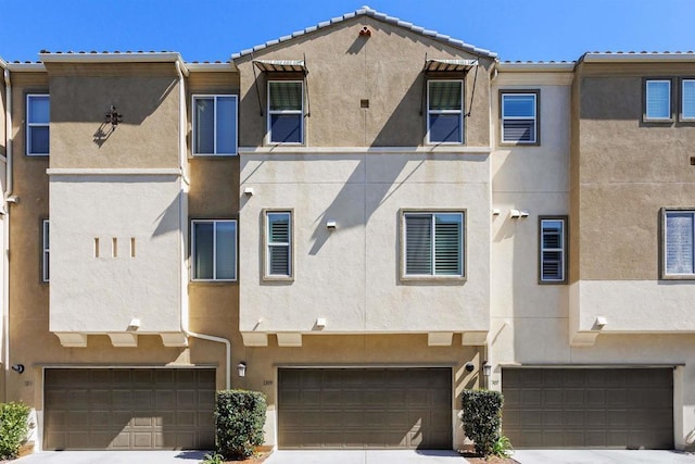 townhome / multi-family property featuring a garage, a tile roof, and stucco siding