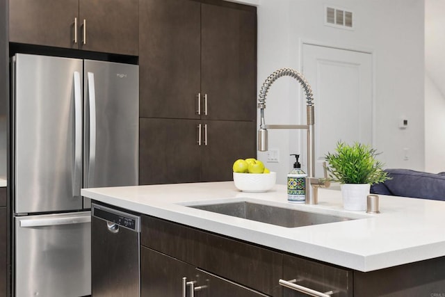 kitchen featuring light countertops, appliances with stainless steel finishes, a sink, and dark brown cabinetry