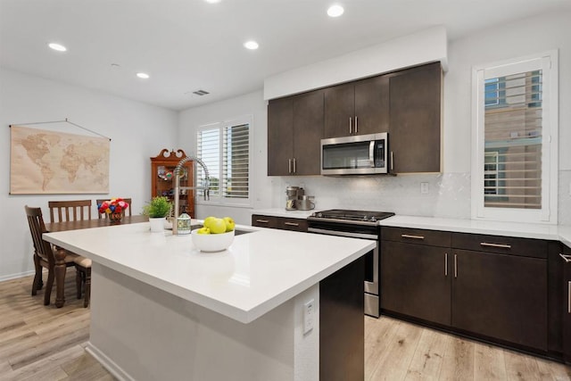 kitchen with visible vents, stainless steel appliances, light countertops, light wood-type flooring, and backsplash