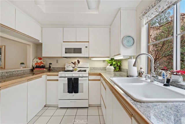 kitchen featuring light tile patterned floors, white appliances, a sink, white cabinets, and a tray ceiling