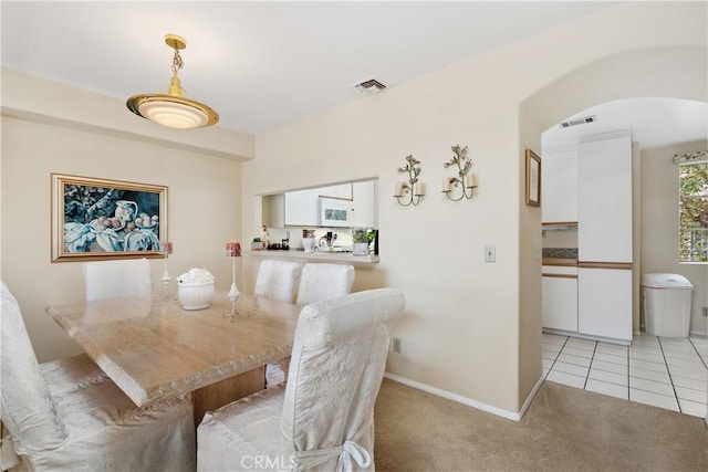 dining room featuring visible vents, arched walkways, baseboards, light colored carpet, and light tile patterned flooring