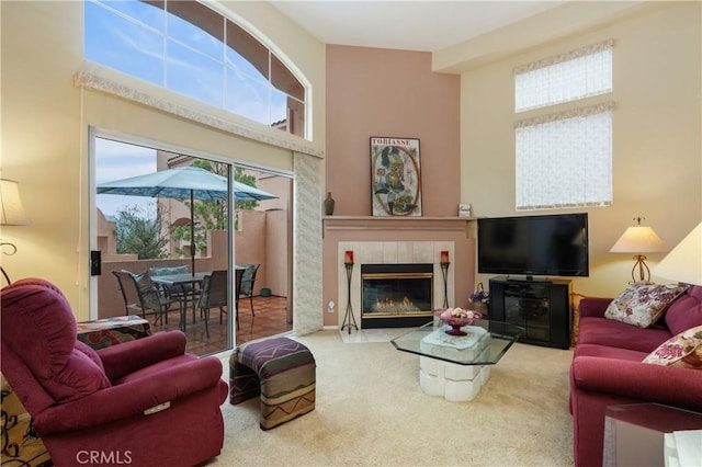 carpeted living room featuring a tile fireplace and a towering ceiling