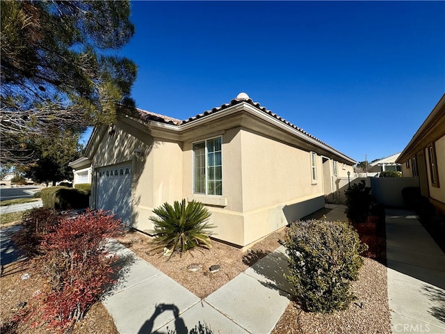 view of side of home featuring a tile roof, fence, an attached garage, and stucco siding