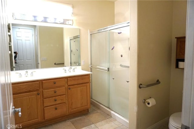 bathroom with double vanity, toilet, a sink, a shower stall, and baseboards