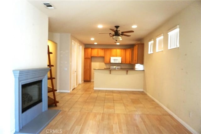 kitchen featuring white microwave, recessed lighting, a peninsula, visible vents, and a glass covered fireplace