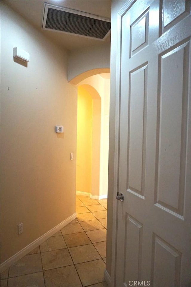 hallway featuring arched walkways, visible vents, baseboards, and light tile patterned flooring