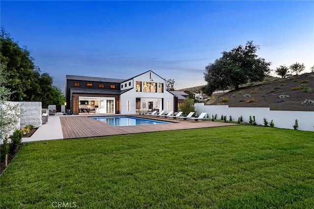 back of property at dusk with a fenced in pool, a lawn, and fence