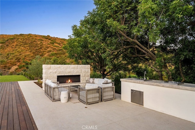 view of patio with an outdoor living space with a fireplace, a deck, a sink, and area for grilling