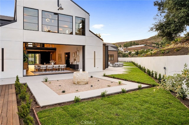 back of house featuring a lawn, a patio area, fence, and stucco siding